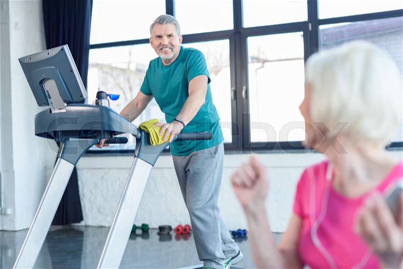 Senior sportsman training on treadmill, senior sportswoman on foreground in senior fitness class , stock photo