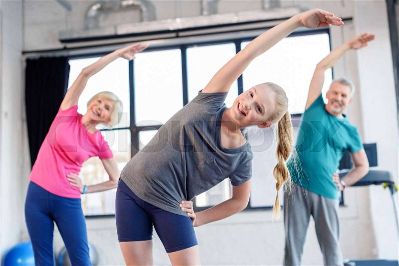 Happy old couple and girl exercising in fitness class for kids and senior people, stock photo