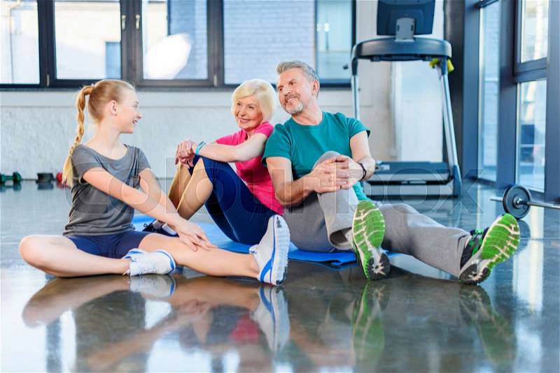 Smiling old couple and girl stretching in fitness class for kids and senior people, stock photo