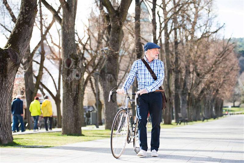 Handsome senior man in blue checked shirt with bicycle in town, looking up. Sunny spring day, stock photo