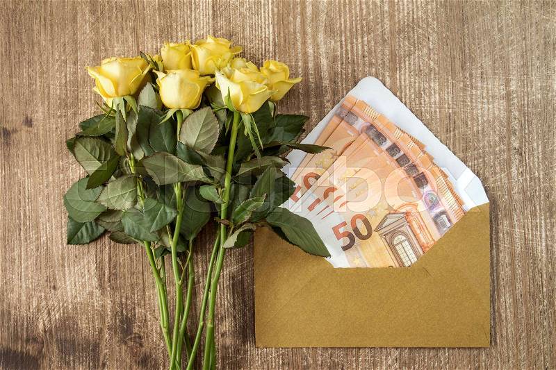 Bunch of roses and envelope with money over wooden background, stock photo