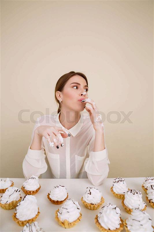 Photo of concentrated young lady posing while eating cupcakes. Isolated and looking aside, stock photo