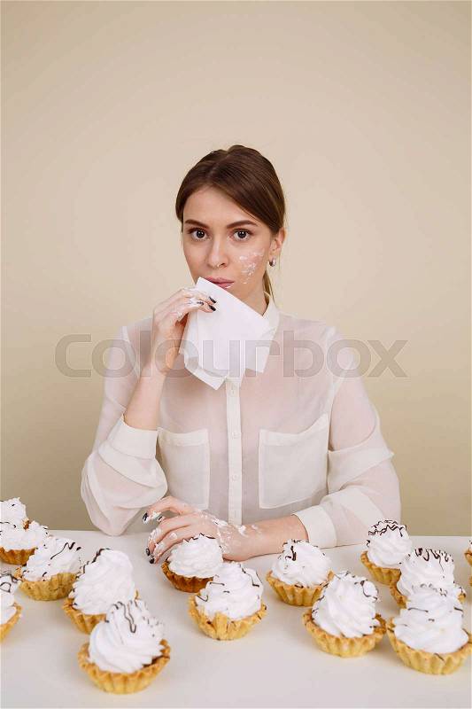 Image of amazing young lady posing while eating cupcakes holding napkin. Isolated and looking at camera, stock photo