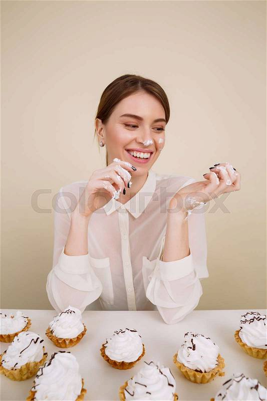 Image of happy young lady posing while eating cupcakes. Isolated and looking aside, stock photo