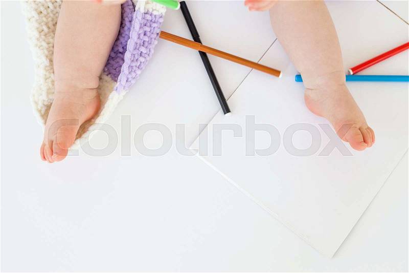 Cropped top view photo of little baby sitting on floor on plaid near markers isolated over white background, stock photo