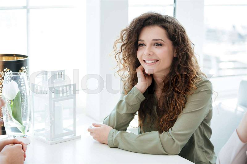 Side view of a happy woman sitting by the table and talking with friend in cafe, stock photo