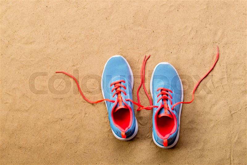 Blue sports shoes with pink shoelaces laid on sand beach background, studio shot, flat lay. Copy space, stock photo