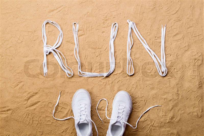 White running shoes and run sign made of shoelaces against sand background, studio shot, flat lay, stock photo