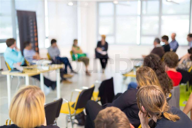 Round table discussion at business and entrepreneurship symposium. Audience in conference hall. Lens focus on unrecognized participant in rear of audience, stock photo