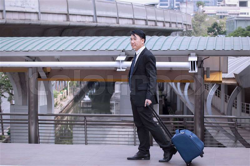 Asian Businessman smiling and happy, wearing suit with luggage, walking on business street for travelling on vacation tourist business trip concept, stock photo
