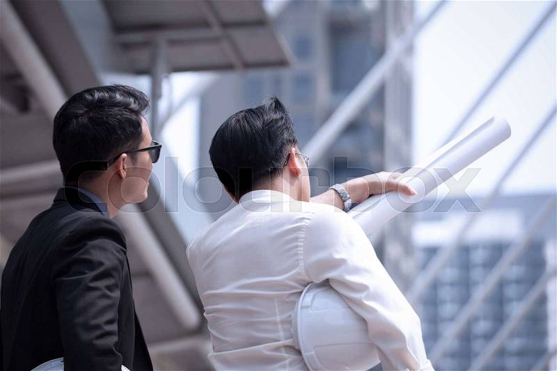 Asian businessman discuss with engineer architect in suite, looking and point to finger forward away and holding construction roll plan for working team concept,back view, stock photo