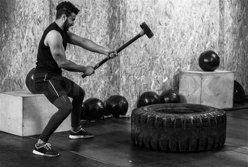 Sport Fitness Man Hitting Wheel Tire With Hammer Sledge Crossfit Training, Young Healthy Guy Gym Interior, stock photo