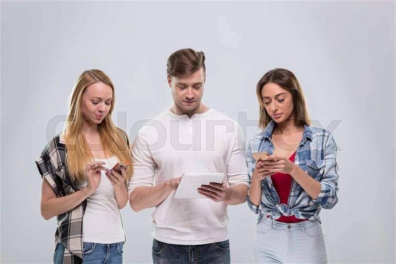 Casual People Group, Young Man Two Woman Happy Smile Using Cell Smart Phone Network Communication Over Grey Background, stock photo