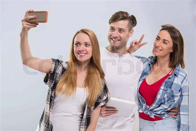 Casual People Group, Young Man Two Woman Happy Smile Taking Selfie Photo Cell Smart Phone Network Communication Over Grey Background, stock photo