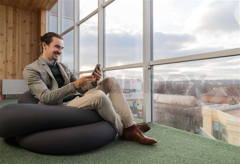 Business Man Using Cell Smart Phone Sit in front Panoramic Window Businessman In Coworking Center Office Interior, stock photo