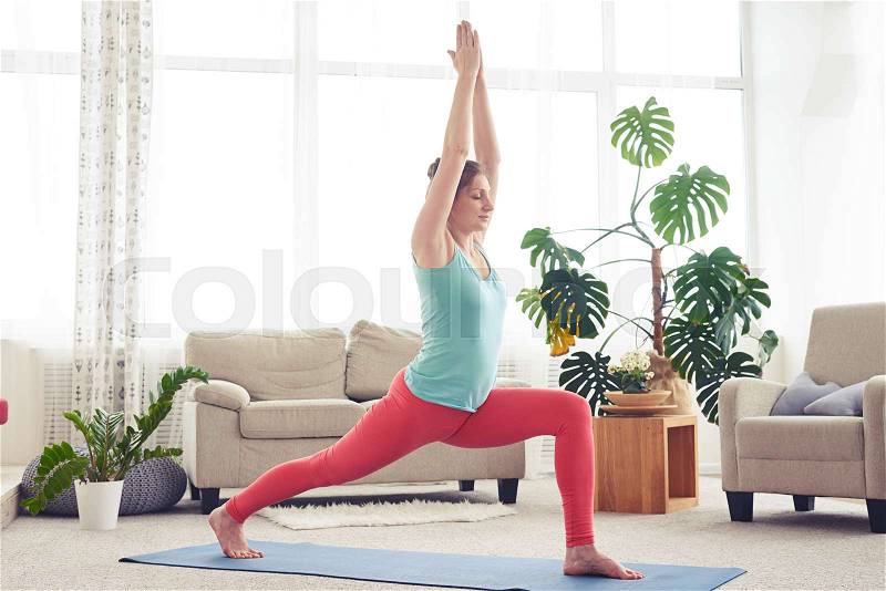 Wide shot of well-built female practicing yoga posture on yoga mat, stock photo