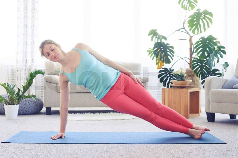 Wide shot of cheerful woman doing side plank pose, stock photo