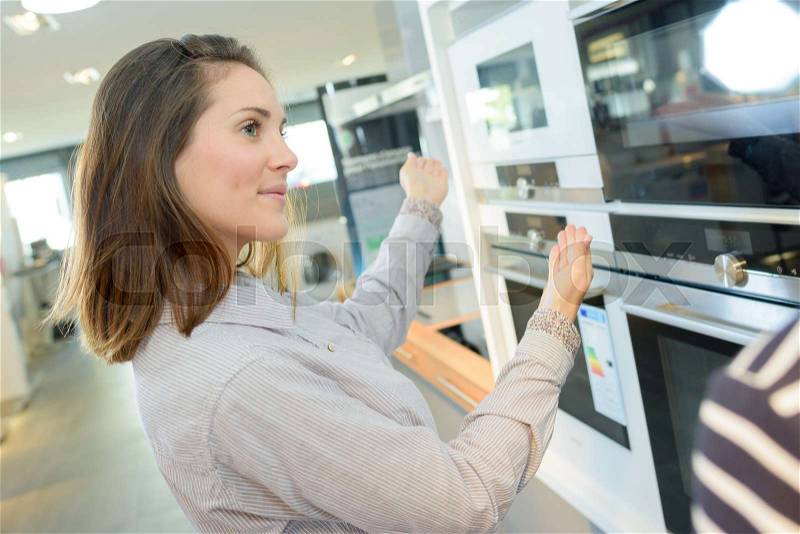 Customer looking at built-in ovens in domestic appliances shop, stock photo