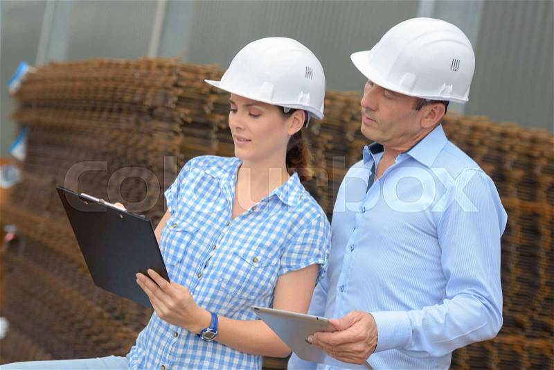 Man and woman looking at clipboard next to building materials, stock photo