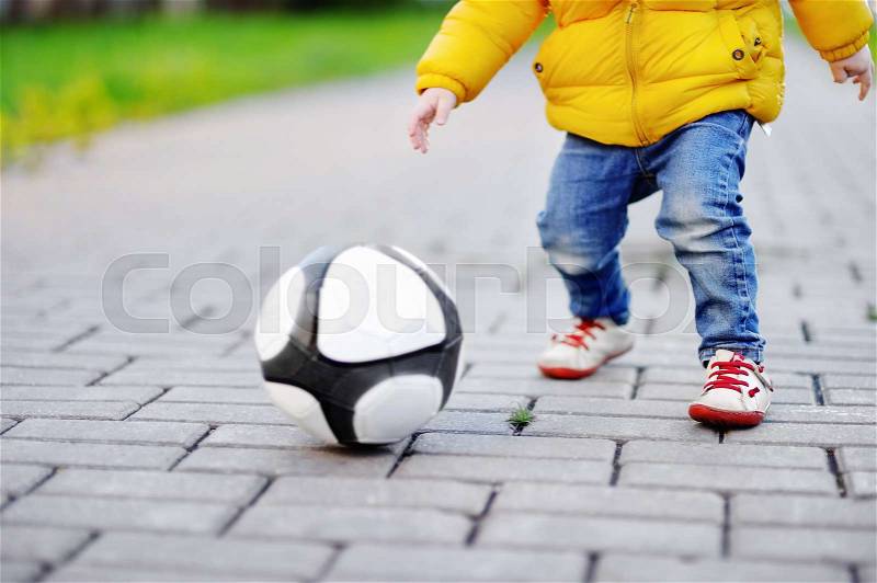 Closeup photo of little boy having fun playing a soccer game on sunny spring or autumn day. Active outdoors game for toddlers, stock photo