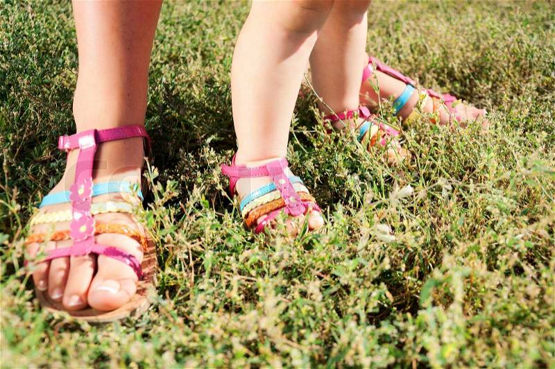 Two pairs of feet in green grass Walking in grass, mother\'s and kid\'s feet in sandals, stock photo
