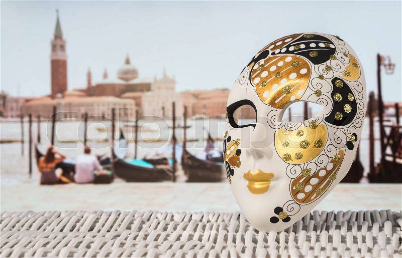 Traditional Venetian Mask with moored gondolas, romantic couple and San Giorgio Maggiore church in the blurred background. Hot summer holiday feeling in beautiful Venice. Authentic travel concept, stock photo
