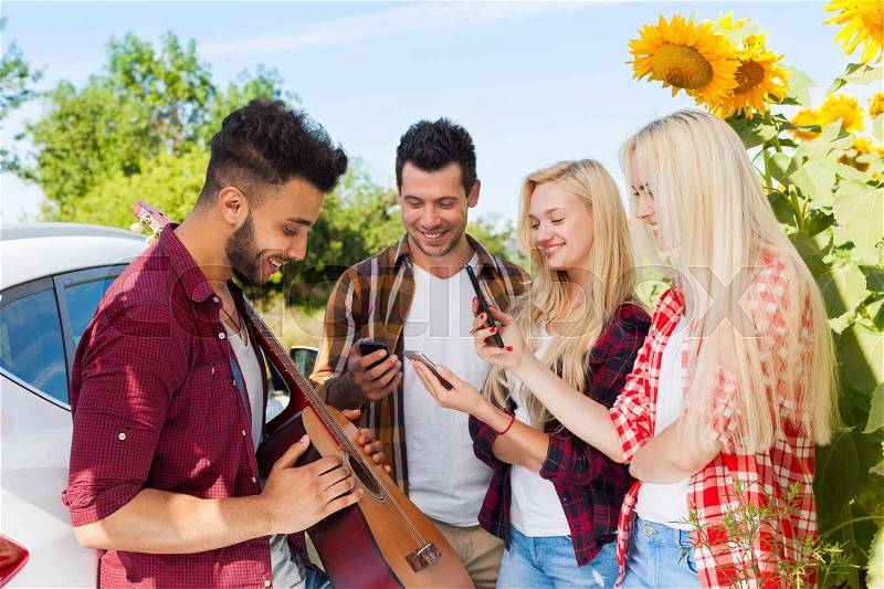 Young people listening guy playing guitar friends drinking beer bottles outdoor countryside, two couple standing near car happy smile summer sunflower, stock photo