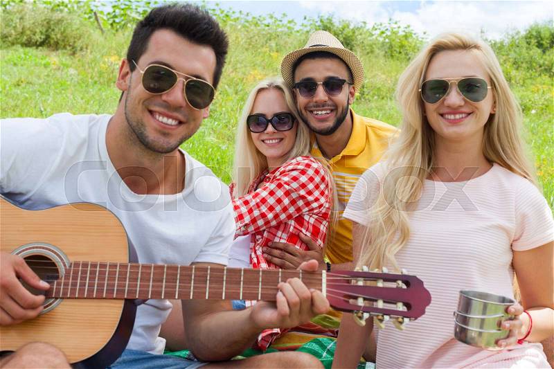 Young people listening guy playing guitar group friends summer day sitting green grass outdoor picnic nature two couple men with girls laugh singing song together, stock photo