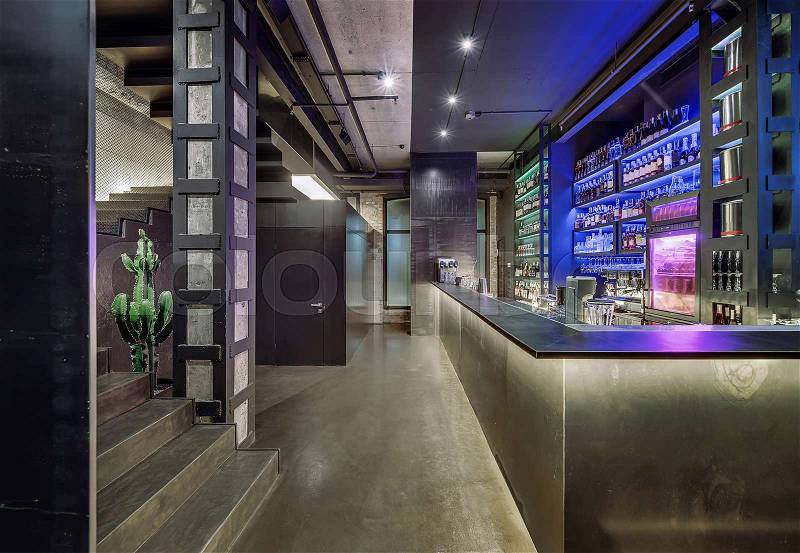 Luminous restaurant in a loft style with brick and concrete walls, column, stairway and a glossy floor. There is a bar rack, shelves with bottles and glasses, fridge, bar equipment, big cactus, stock photo