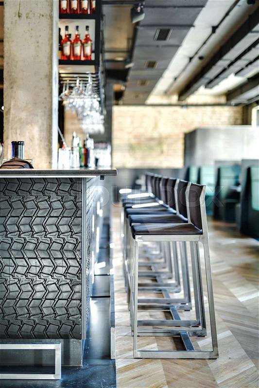 Trendy restaurant in a loft style with brick walls and a concrete column. There is a dark textured bar rack with chairs, shelves with bottles and glasses, sofas with tables and partitions. Vertical, stock photo