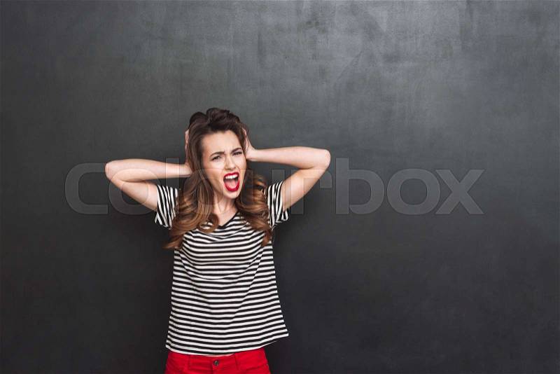 Screaming woman covering her ears and looking at the camera over black background, stock photo