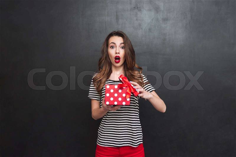 Shocked woman opening a gift box and looking at the camera over black background, stock photo