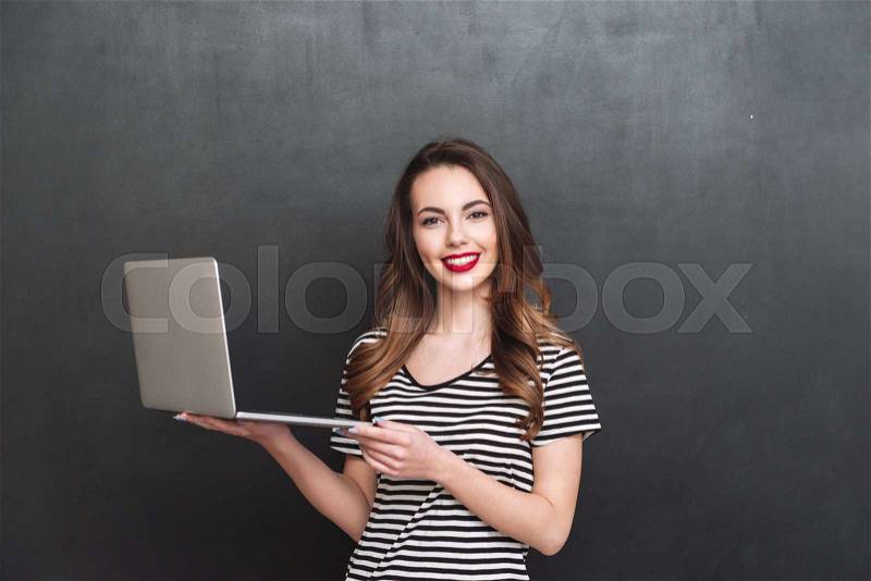 Smiling woman holding laptop computer and looking at the camera over black background, stock photo