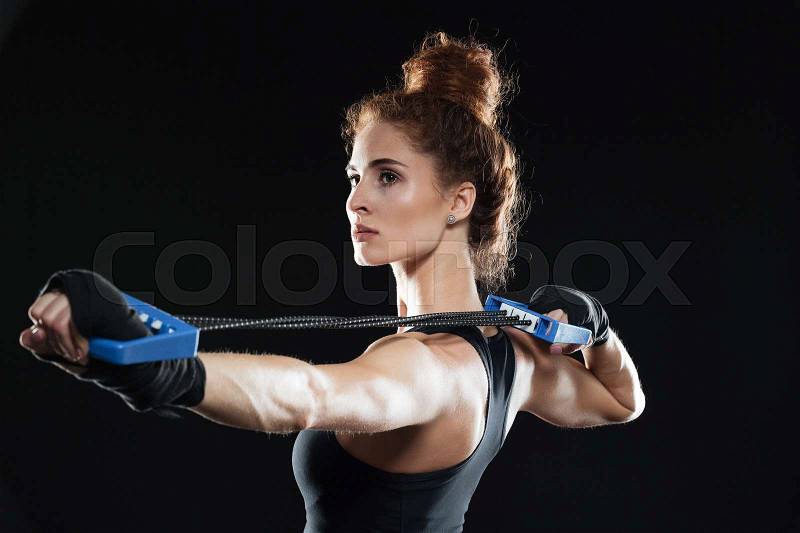 Side view of a female fighter using expander over black background, stock photo