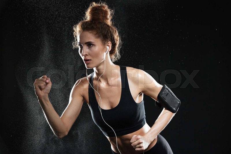 Concentrated fitness woman running in studio over black background, stock photo