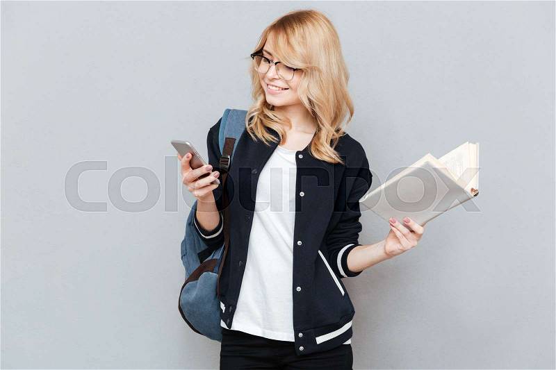 Cute female student using phone and holding book in hands isolated, stock photo