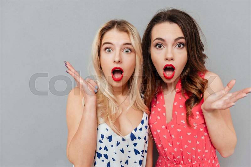 Image of shocked young two ladies friends with bright makeup lips standing over grey wall and posing. Looking at camera, stock photo