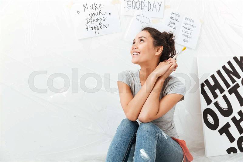 Picture of dreaming young lady artist sitting on floor over white background. Looking aside, stock photo