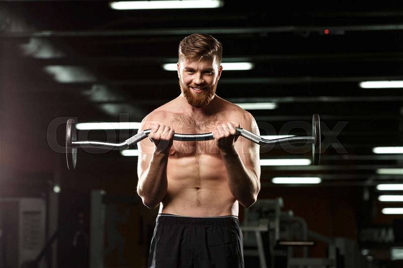 Image of happy sports man make sport exercises with barbell in gym and looking at camera, stock photo