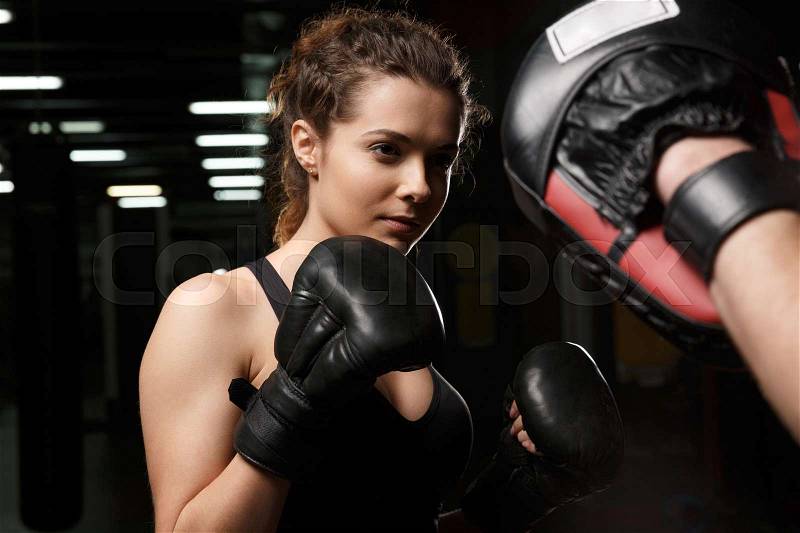 Picture of concentrated young strong sports lady boxer standing in gym with man trainer and looking aside, stock photo