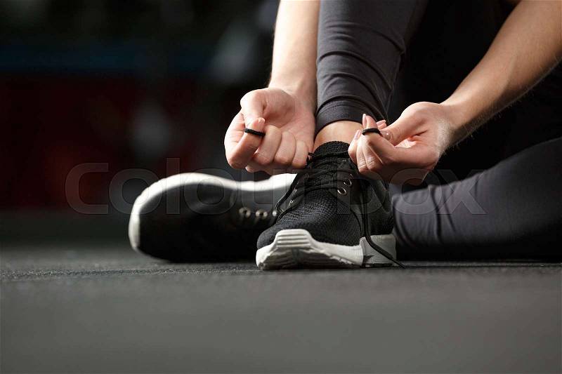 Cropped image of young strong fitness lady sitting and tie laces in gym, stock photo