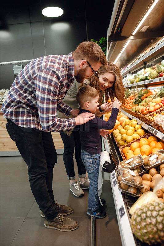 Vertical image of a family playing with citrus in supermarket. Side view, stock photo