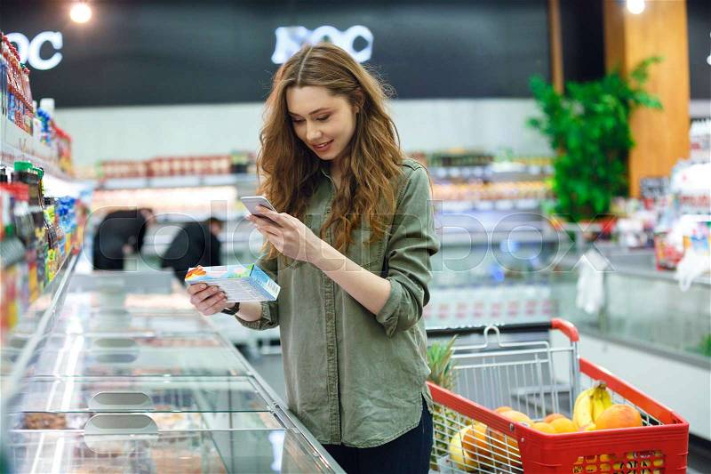 Cheerful brunette woman photographing product in supermarket, stock photo