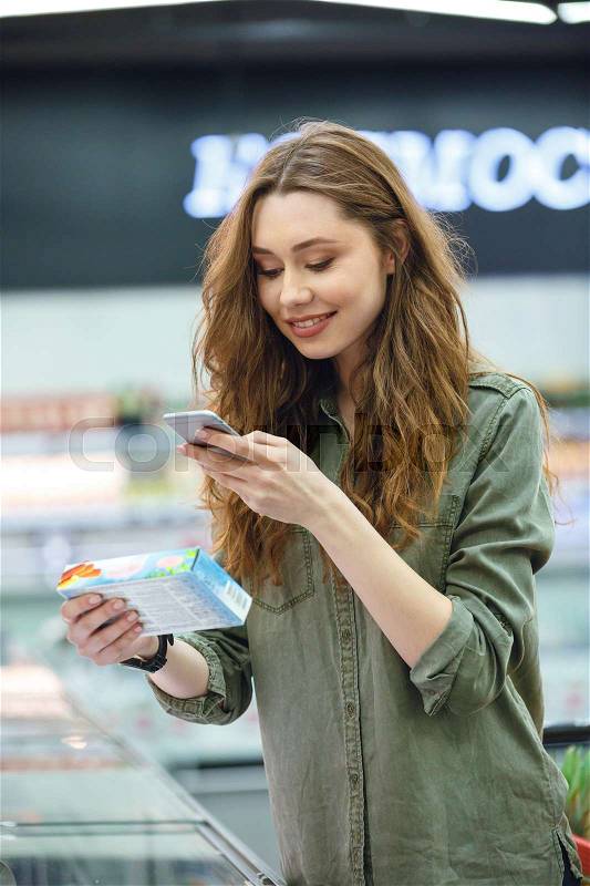 Shot of funny brunette woman photographing product in supermarket, stock photo