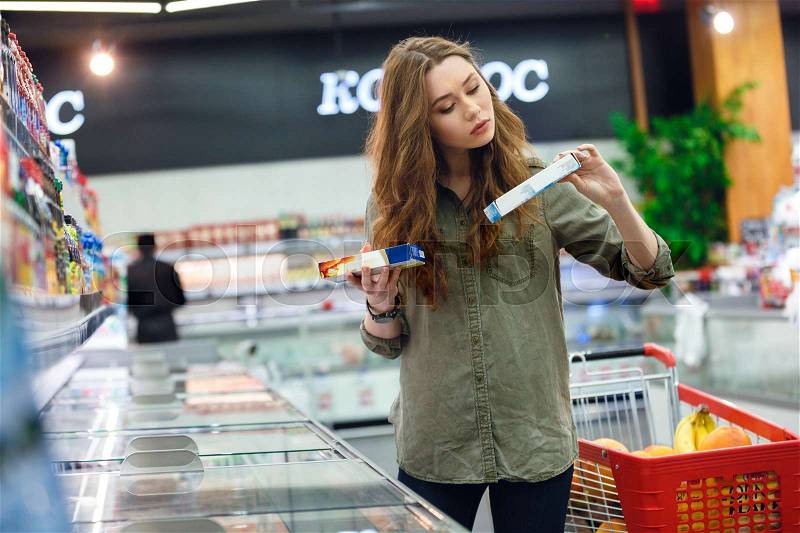 Young woman buyer trying to make choice between two products in shopping centre, stock photo