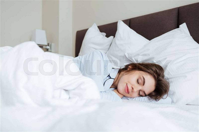 Photo of cheerful young lady dressed in pajama lies in bed at home under a blanket sleeping, stock photo