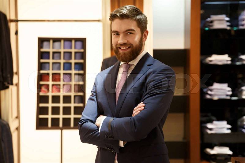 Smiling bearded man in suit standing with crossed arms in a shop and looking at the camera, stock photo