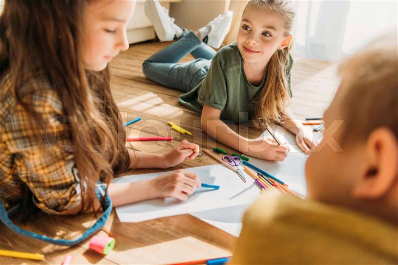 Cute kids drawing on paper with pencils while lying on floor, stock photo