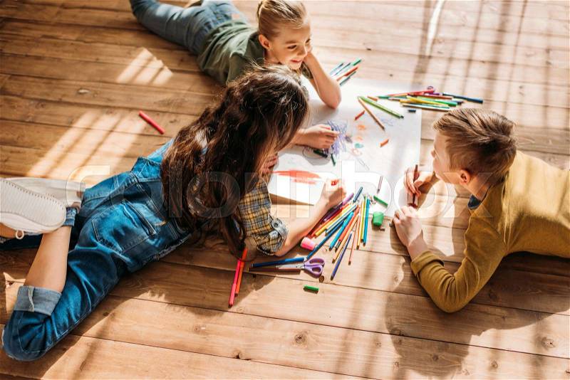 Cute kids drawing on paper with pencils while lying on floor, stock photo