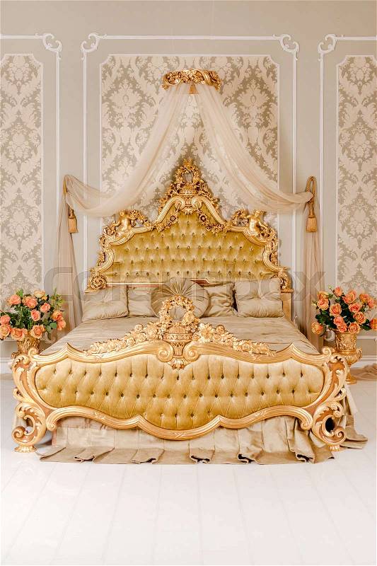 Luxury bedroom in light colors with golden furniture details. Big comfortable double royal bed in elegant classic interior, stock photo